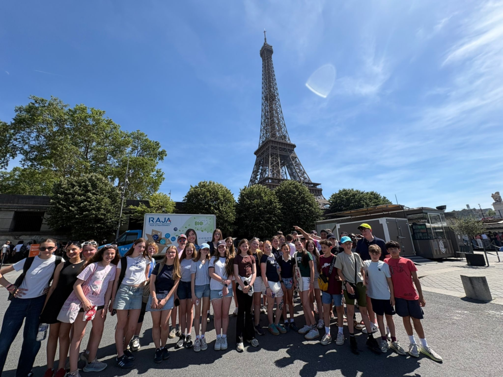 Group of students posing for a photo in front of the Eiffel Tower on a sunny day with blue sky.