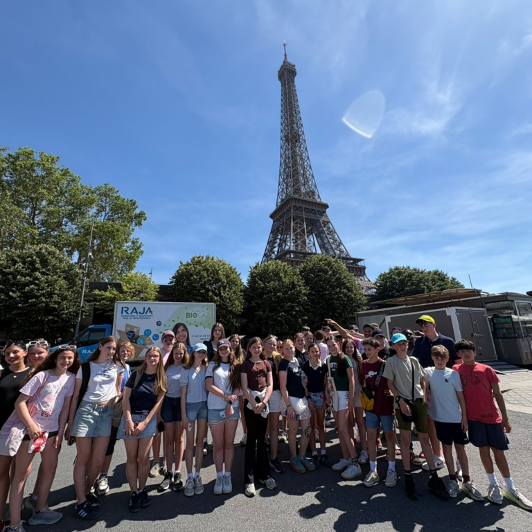 Group of students posing for a photo in front of the Eiffel Tower on a sunny day with blue sky.